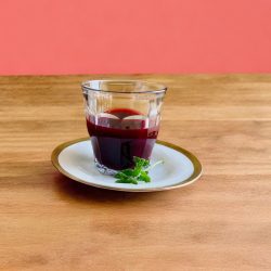 Granatapfelsaft im Glas auf Holztisch vor lachsfarbenem Hintergrund
